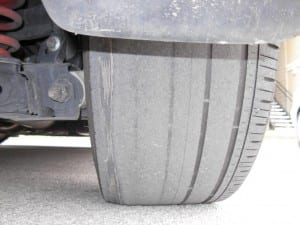 Close-up view of a severely worn, bald car tire showing uneven tread wear and exposed steel belts on the inner edge.
